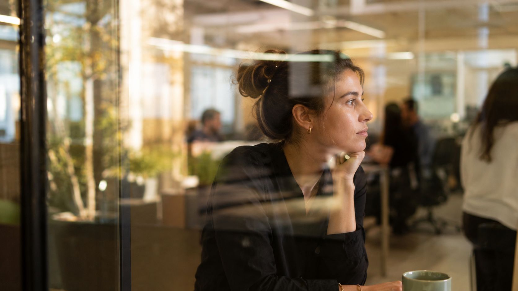 A woman in a black shirt sitting in an office, gazing thoughtfully while resting her chin.