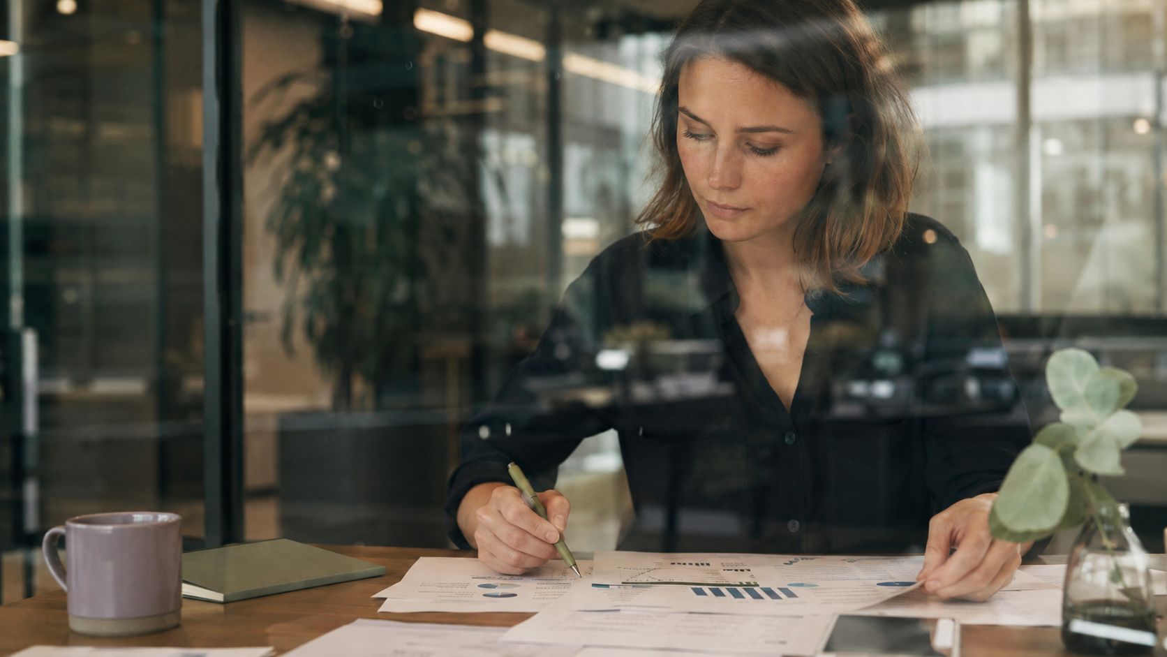 A focused businesswoman analyzes financial reports and charts while working at her desk in a modern office.