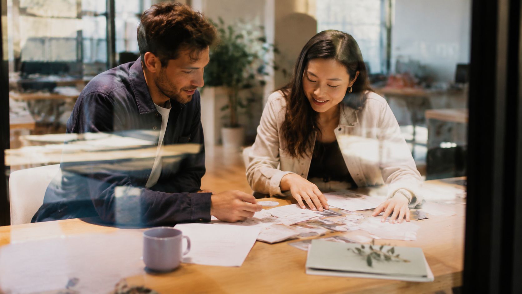 A man and a woman collaborating on a project together at a wooden table in an office.