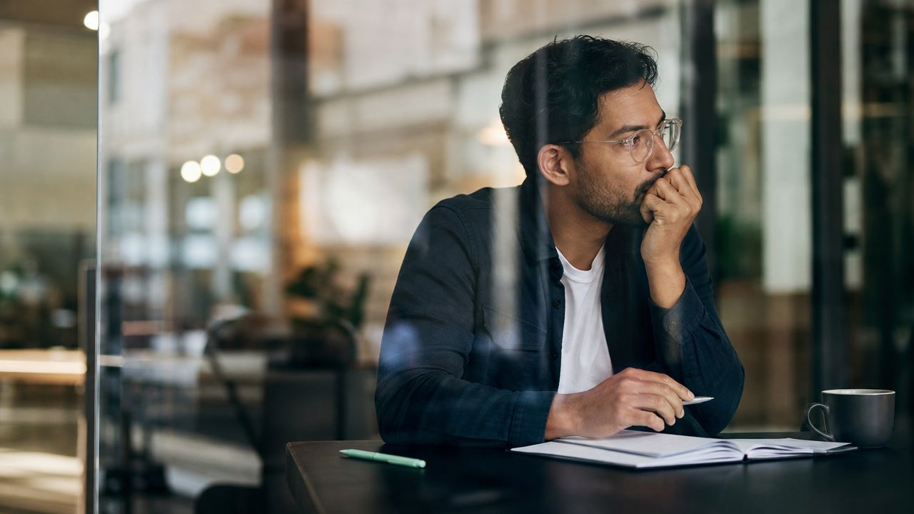 A thoughtful professional man sitting at a desk with a notebook while contemplating his business strategy.