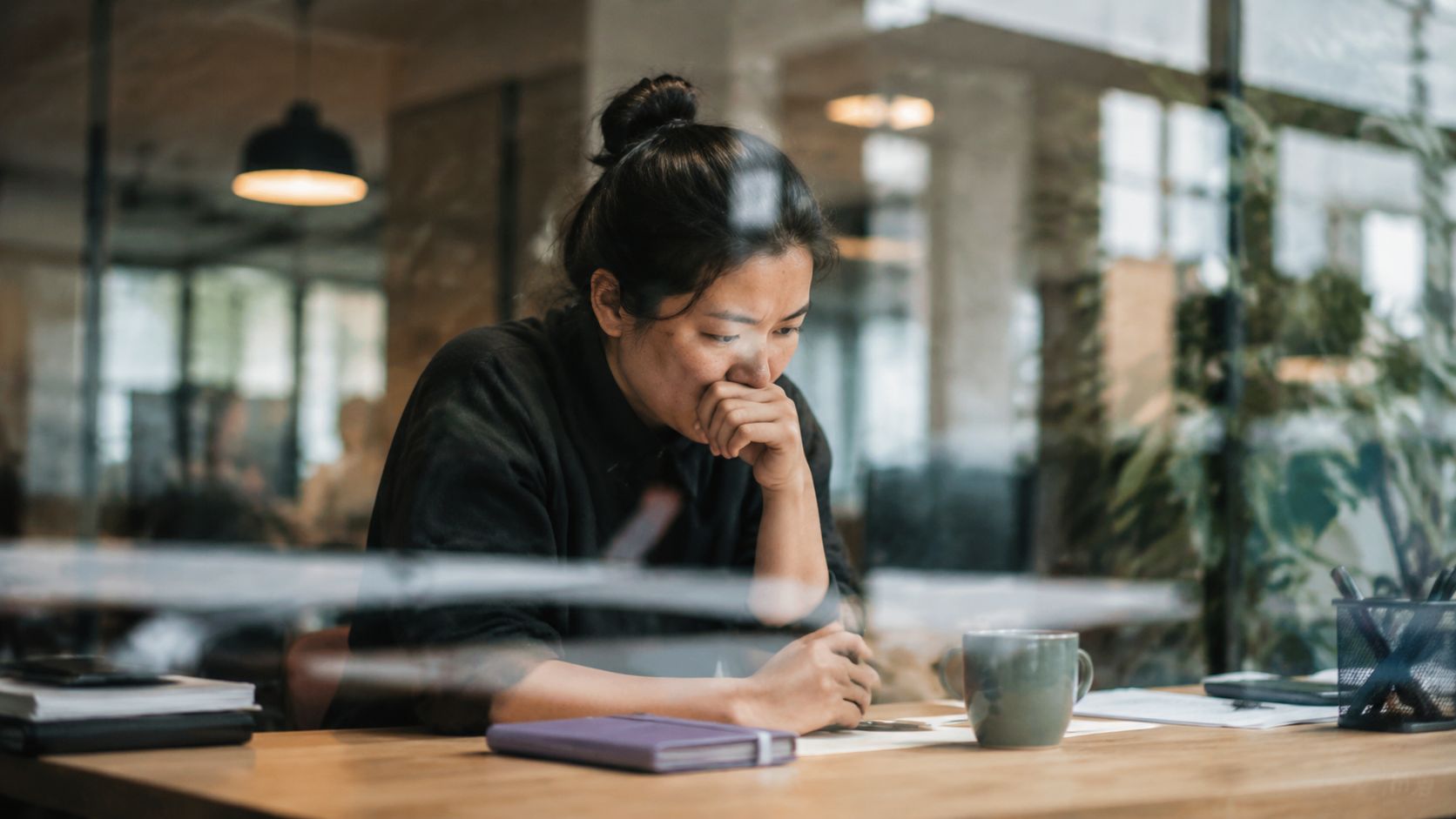 A focused woman sitting at a desk in an office environment, deep in thought while working.