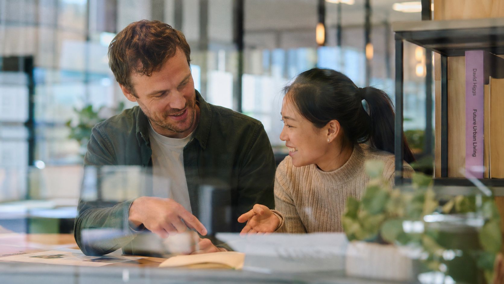 A professional man and woman collaborating together in a modern office while discussing business documents.