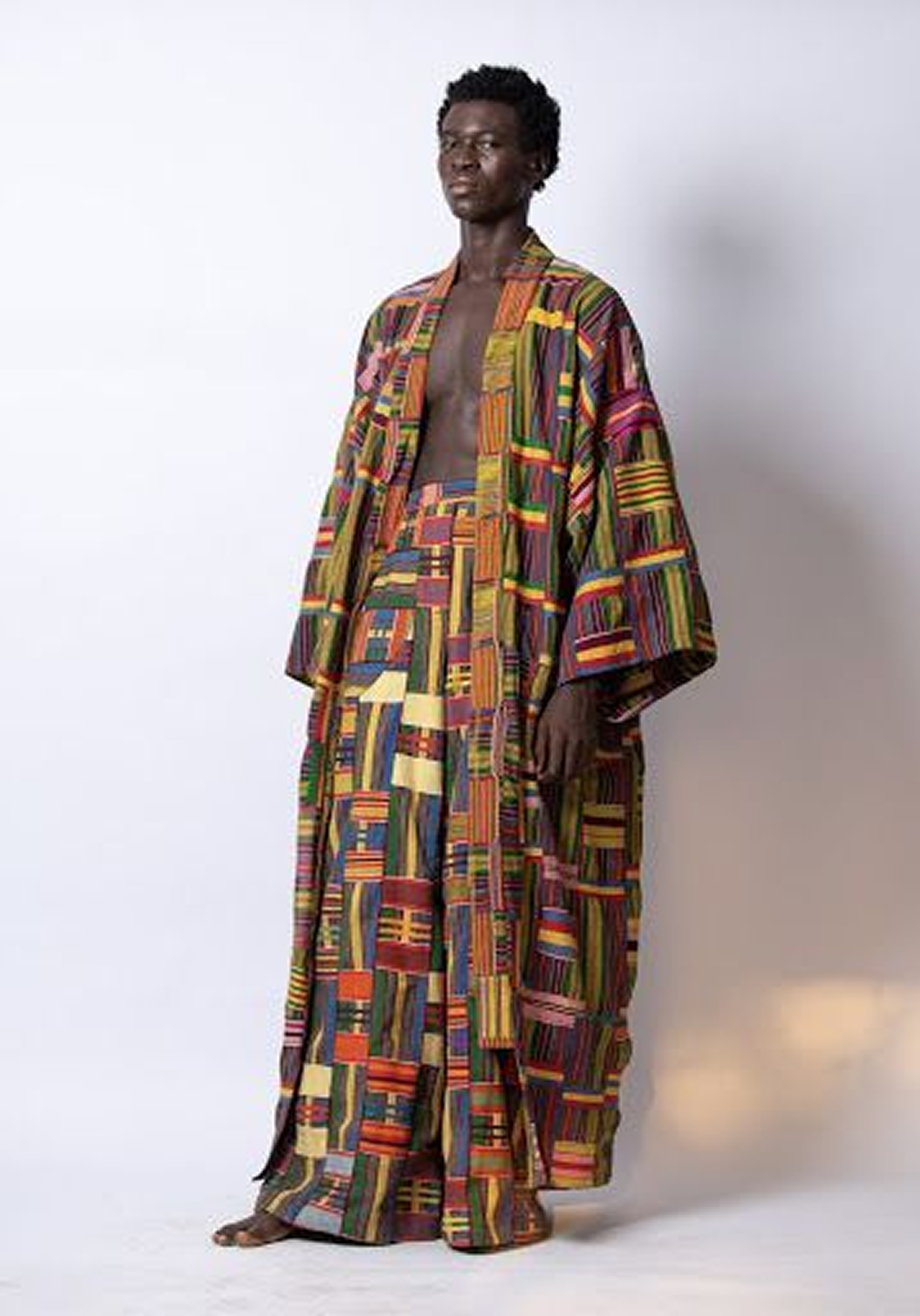 Man wearing a colorful, patterned wide-sleeve robe and matching wide-leg pants against a plain light background.