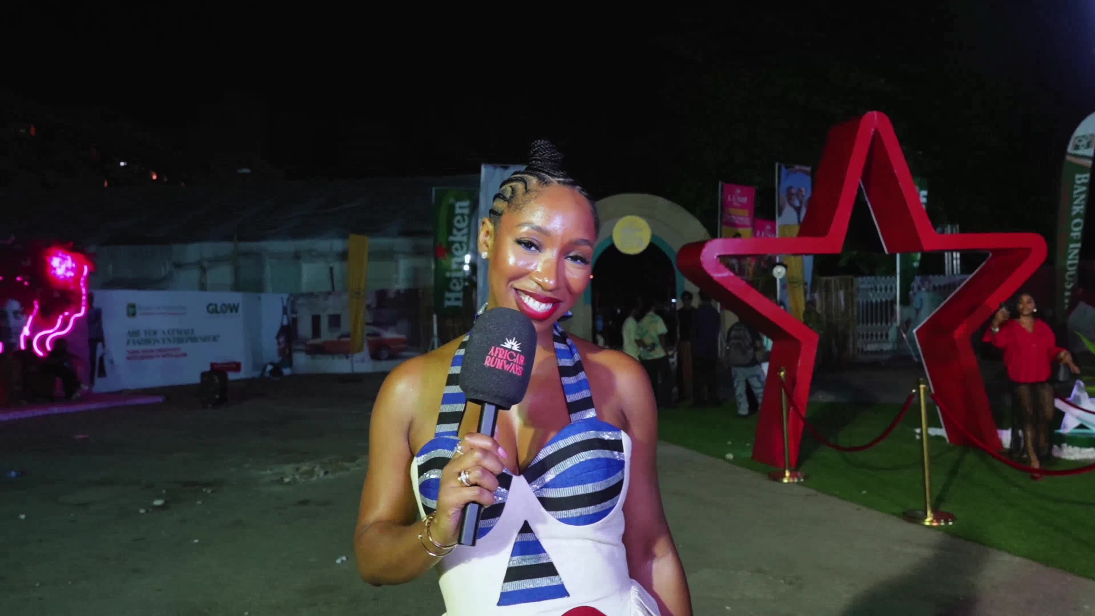 Smiling woman with braided hair holding a microphone branded African Runways at an outdoor nighttime event.
