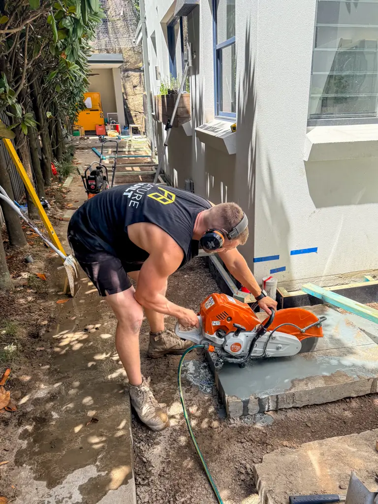 Construction worker wearing ear protection cutting a concrete slab outdoors with a power saw.