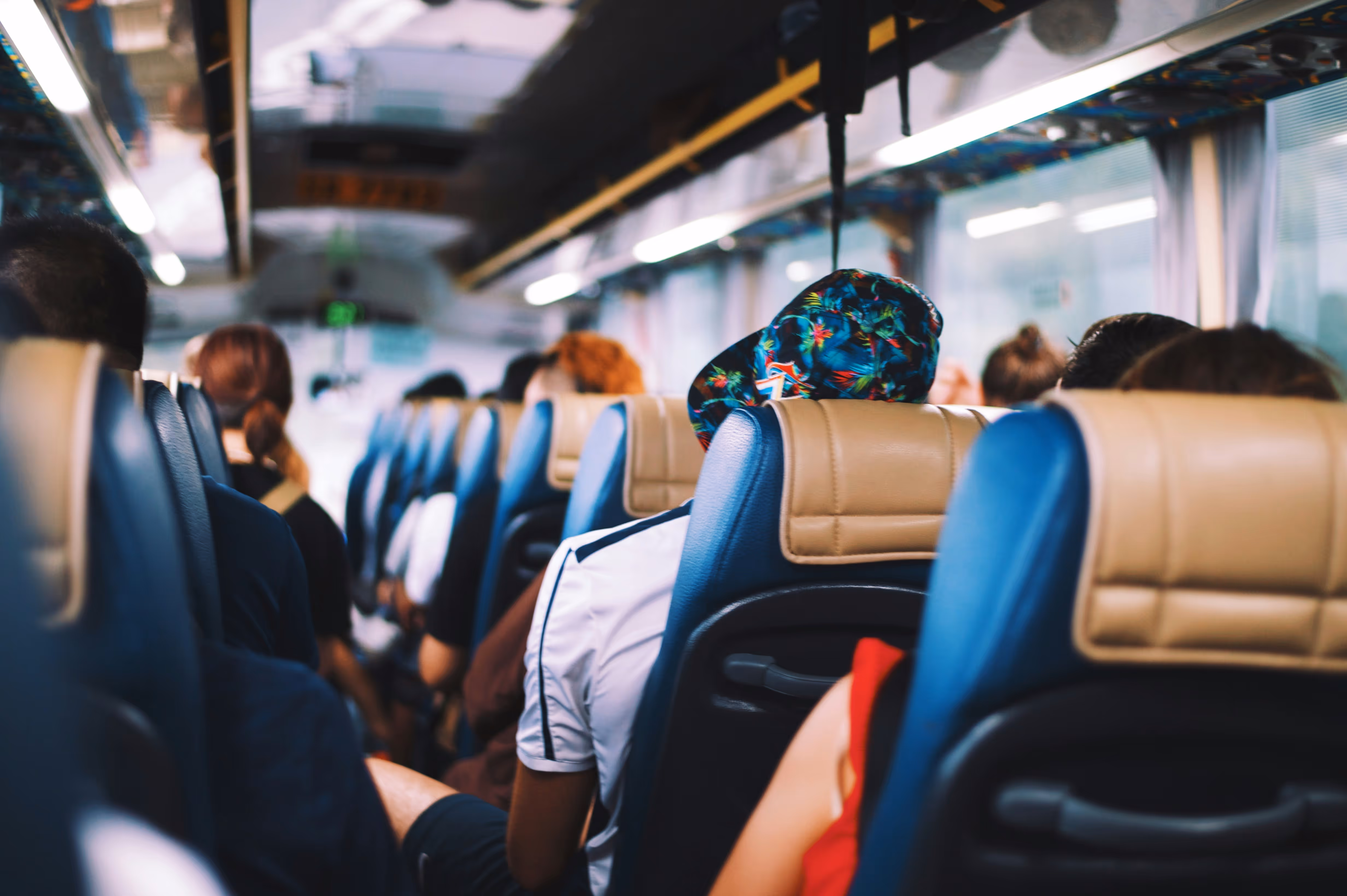 Passengers seated inside a bus viewed from the back rows with headrests and windows visible.
