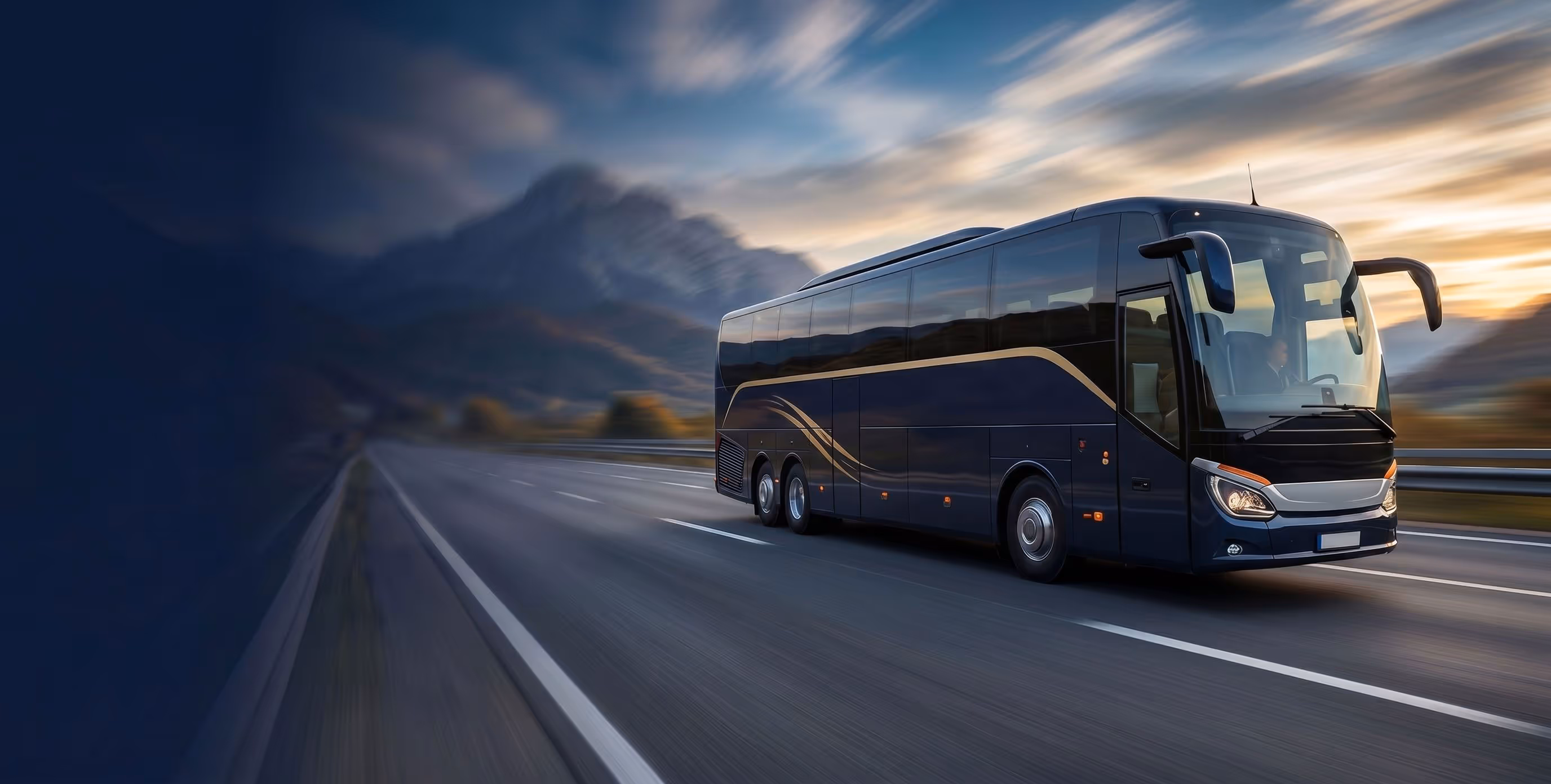 Modern dark blue coach bus driving on an empty highway with mountains and a cloudy sunset sky.
