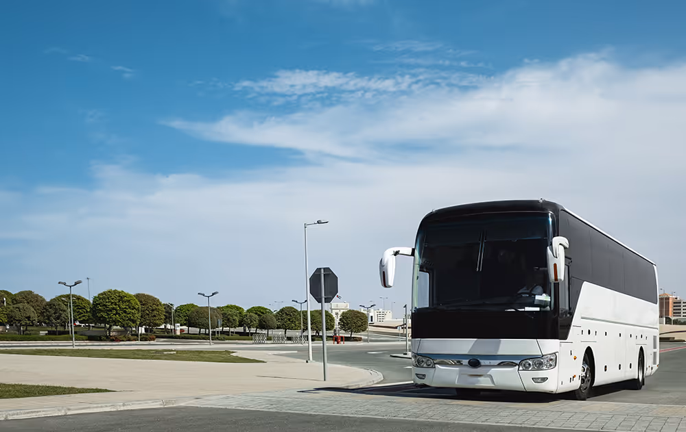 White and black coach bus parked on a road under a partly cloudy sky.