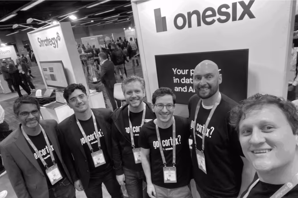 Group selfie of six men wearing 'go cortex? onesix' shirts at a trade show booth with 'onesix' and 'Strategy8' signage in the background.