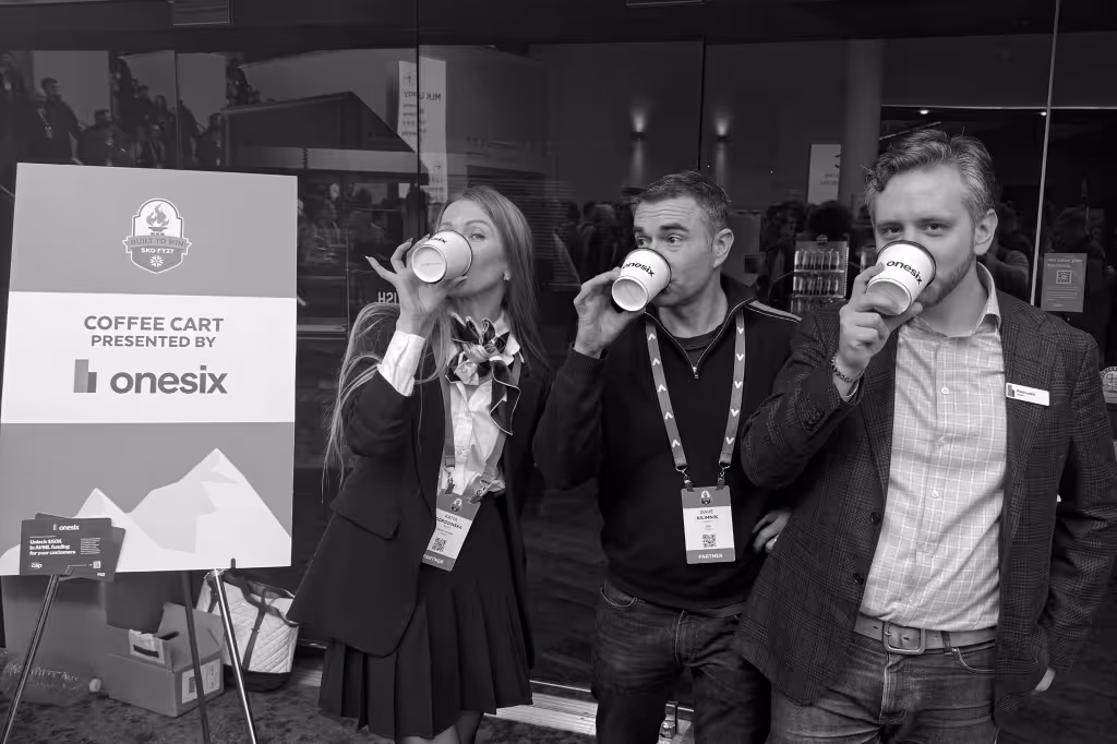 Three people standing and drinking coffee from onesix branded cups near a coffee cart sign.