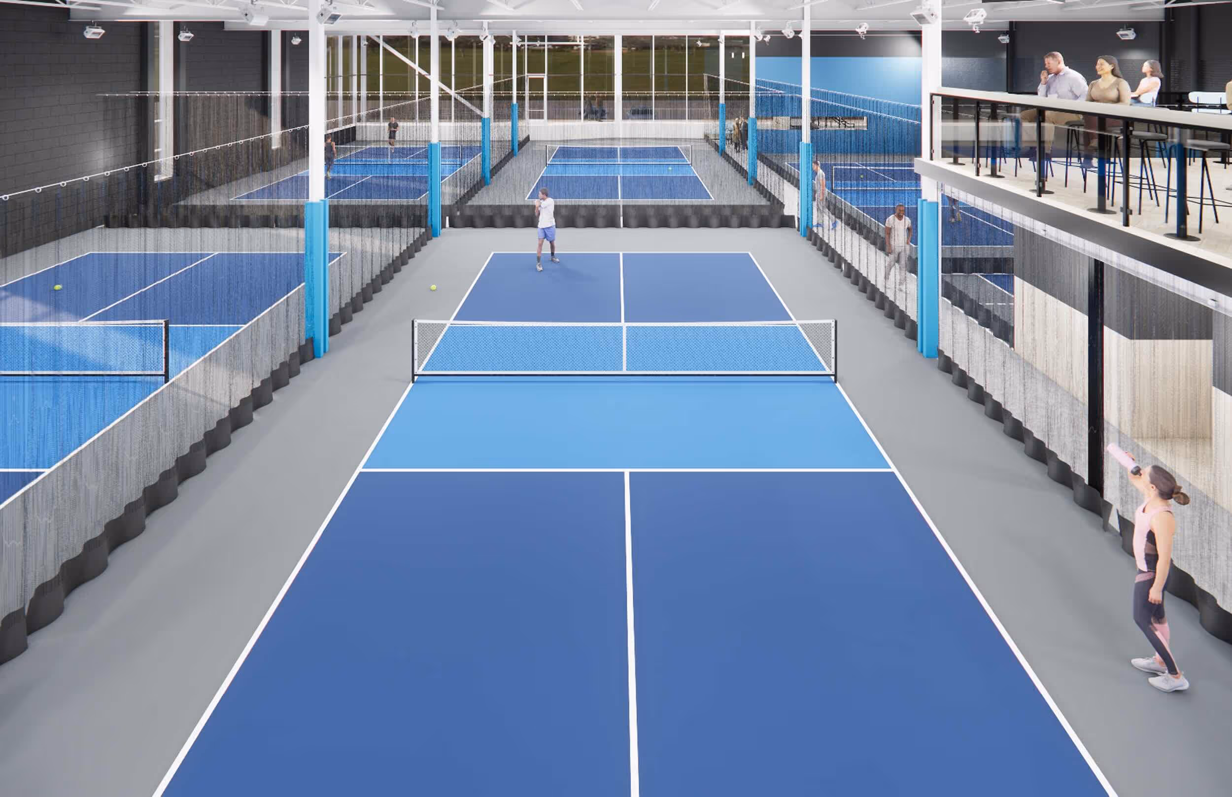 Indoor pickleball courts with players on courts and spectators in an elevated seating area.