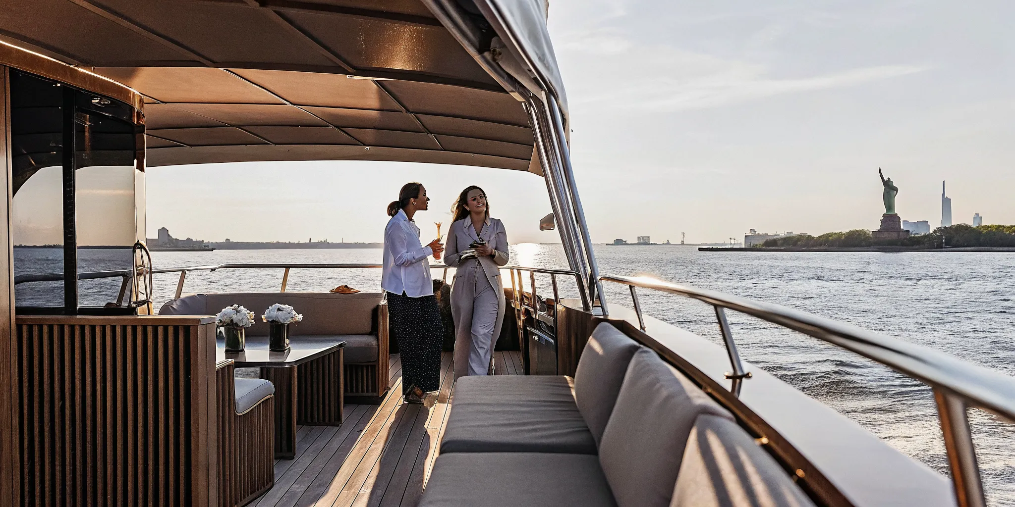 Private luxury yacht cruising the Hudson River with Manhattan skyline and Statue of Liberty at sunset