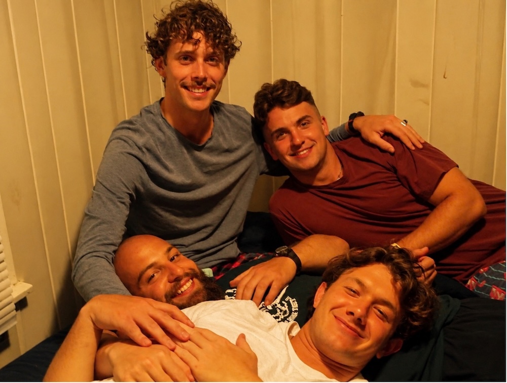 Four AmeriCamp summer camp counsellors smiling and relaxing together inside a cabin at an American summer camp.