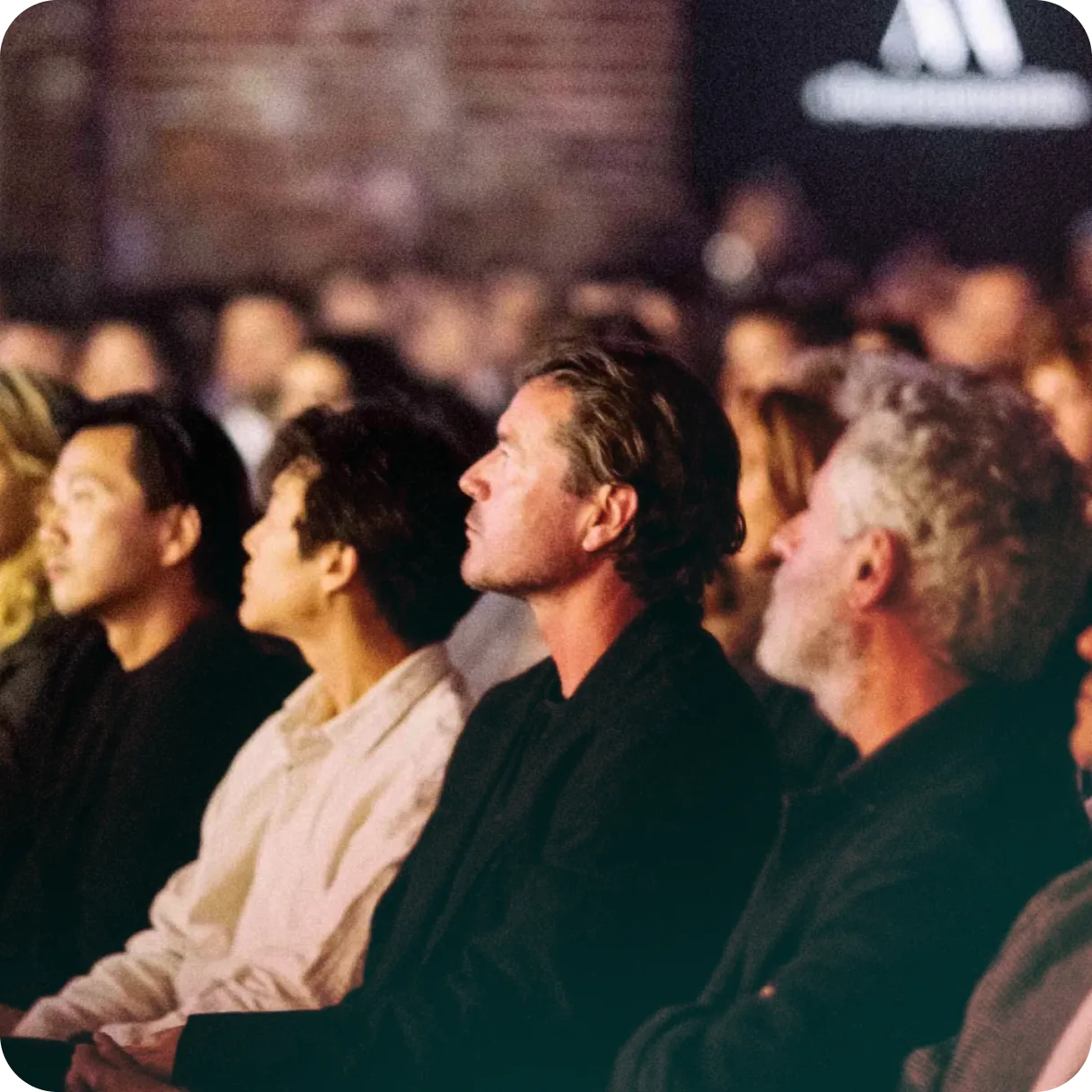 Audience seated and attentively watching an event, with several men in focus in the front row.