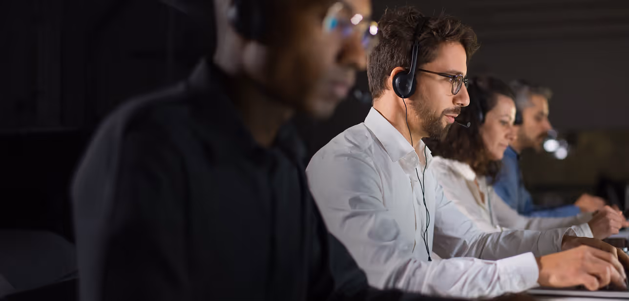 Row of call center operators wearing headsets, focused on their work at computers.