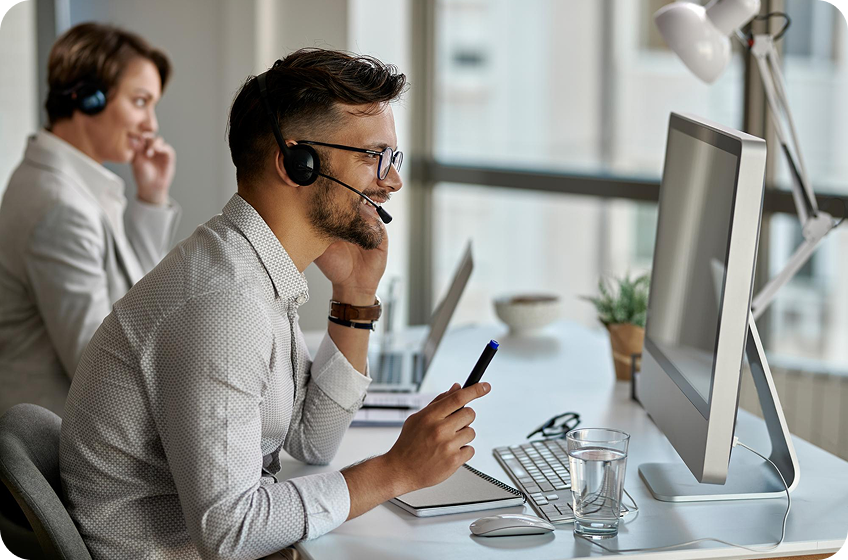 Two call center workers with headsets using computers in a modern office environment.