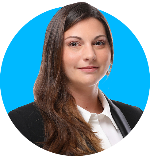 Portrait of a woman with long brown hair in a black blazer and white shirt on blue background.