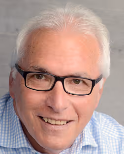 Smiling older man with white hair and glasses wearing a blue checkered shirt.