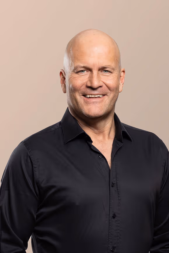 Smiling bald man wearing a black button-up shirt against a beige background.