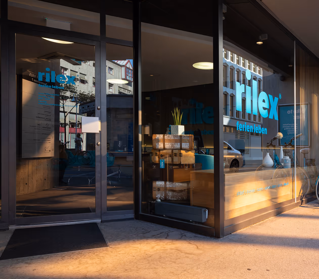 Travel agency storefront with stacked vintage suitcases and blue 'rilex ferien leben' logo on glass.
