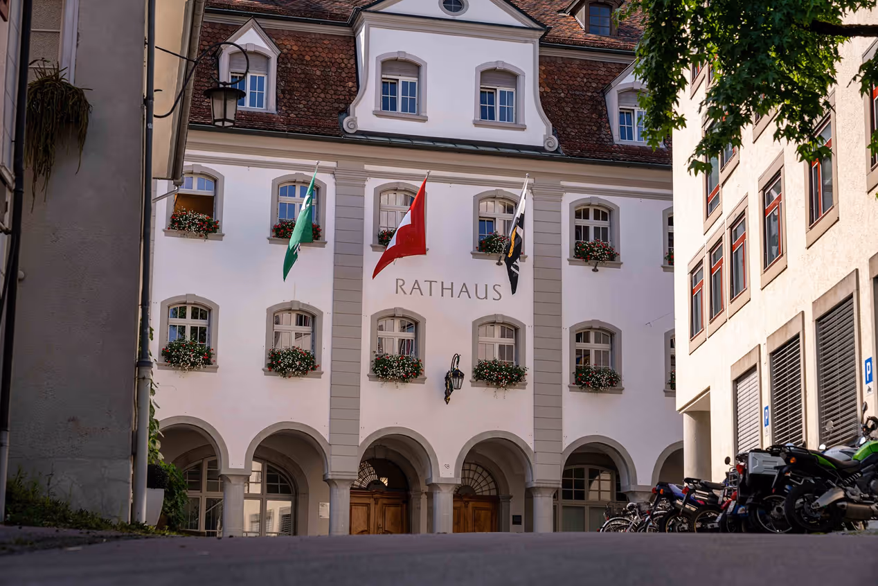 Historic Rathaus building with arched entrances, flower boxes under windows, and three flags on facade.