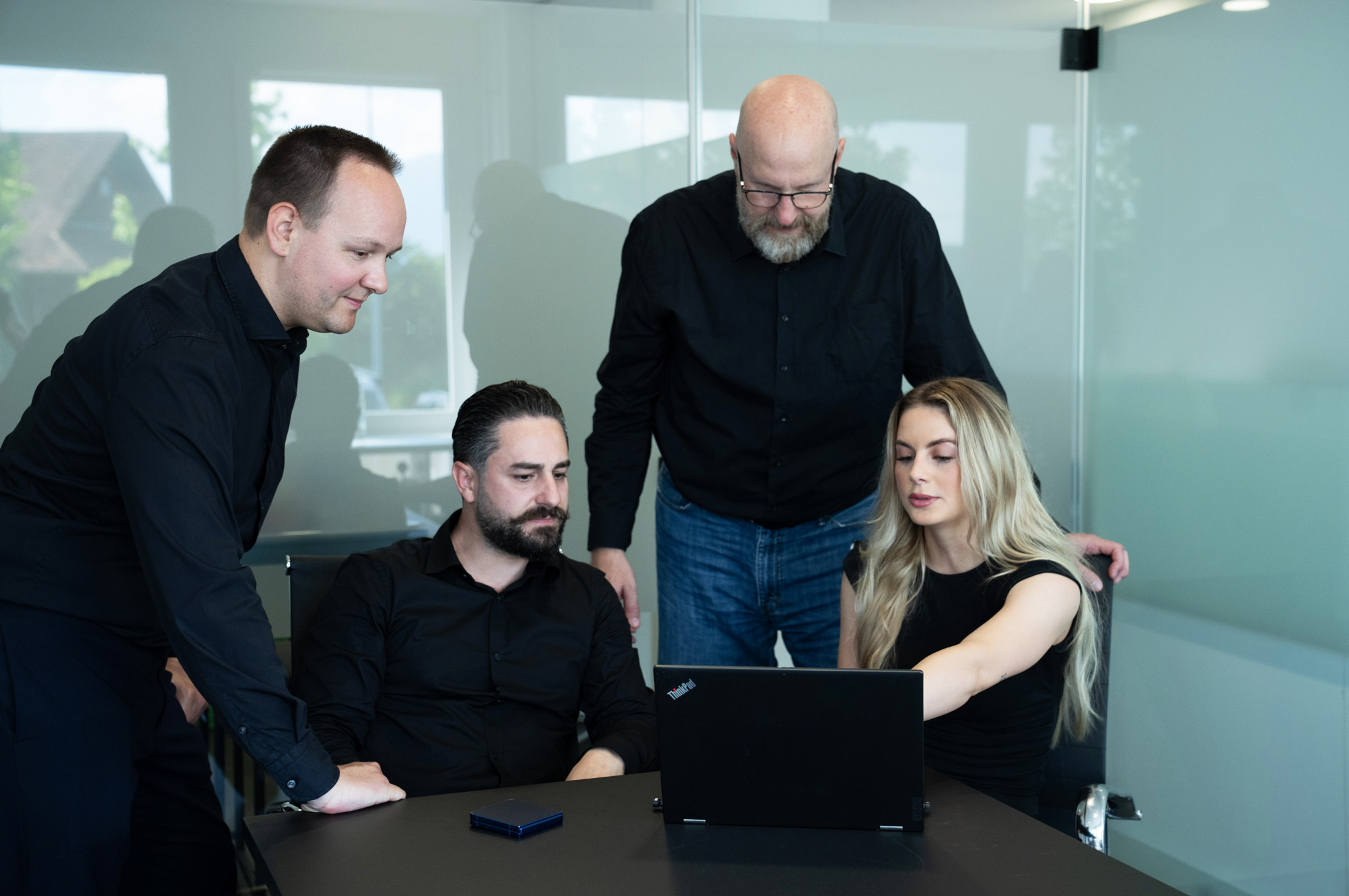 Three people in a meeting room with laptops and glasses of water, smiling and talking.