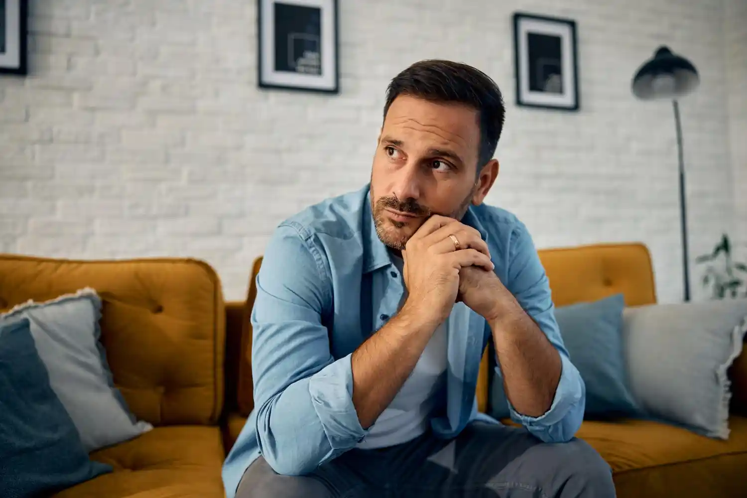 A calm, introspective scene showing a person sitting on a couch, appearing thoughtful or slightly concerned. Soft natural light creating a gentle, emotional mood.