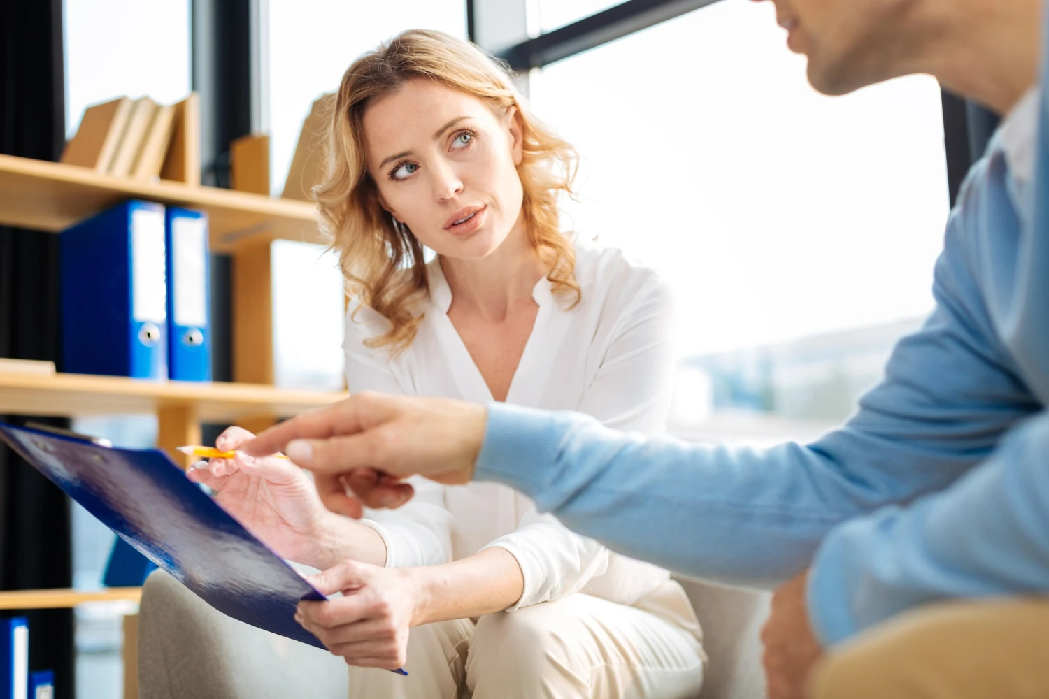 One Women and one man are sitting in chairs in a waiting room. The woman on the left is explaining a picture.