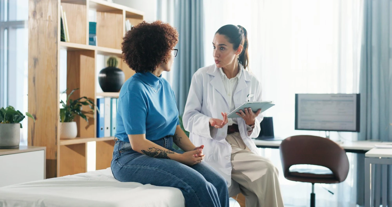 A clean, modern medical setting with a calm, reassuring atmosphere. A female doctor consulting a patient in a bright room.