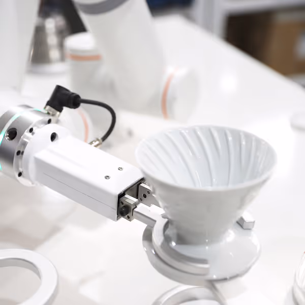 Close-up of a robotic arm holding a white coffee dripper with a metal clamp.