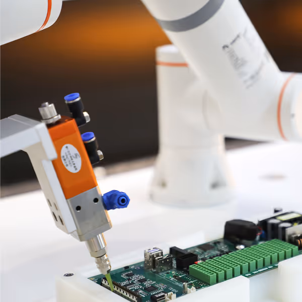 Robotic arm soldering components on a green electronic circuit board.