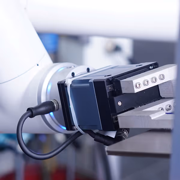 Close-up of a robotic arm with a mechanical gripper holding a flat metallic object.