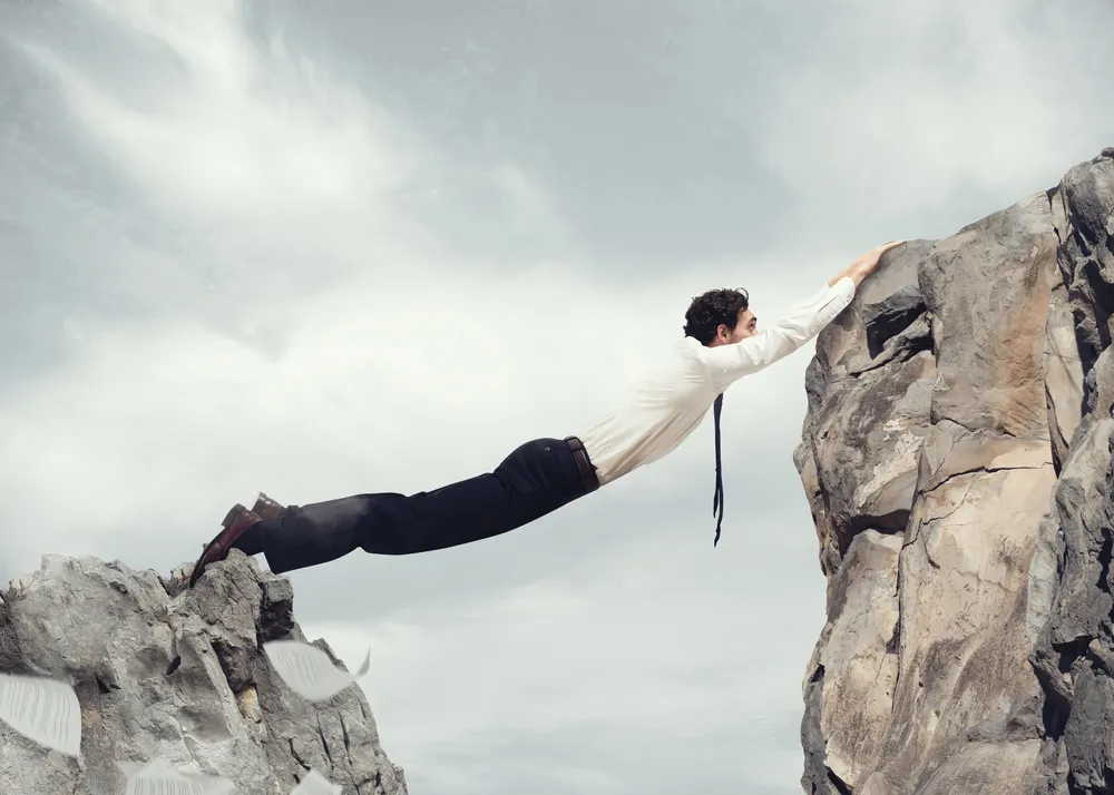 Mann springt über eine Lücke zwischen zwei Felsen und hält sich an der Felskante fest