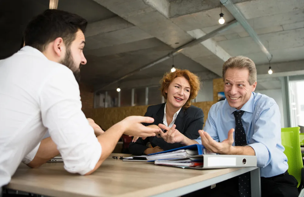 Drei Personen diskutieren lachend an einem Bürotisch