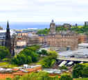 Cityscape of historic buildings and greenery under a cloudy sky near a waterfront.