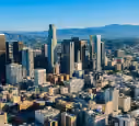 Downtown cityscape with tall skyscrapers and mountains in the background under a clear sky.