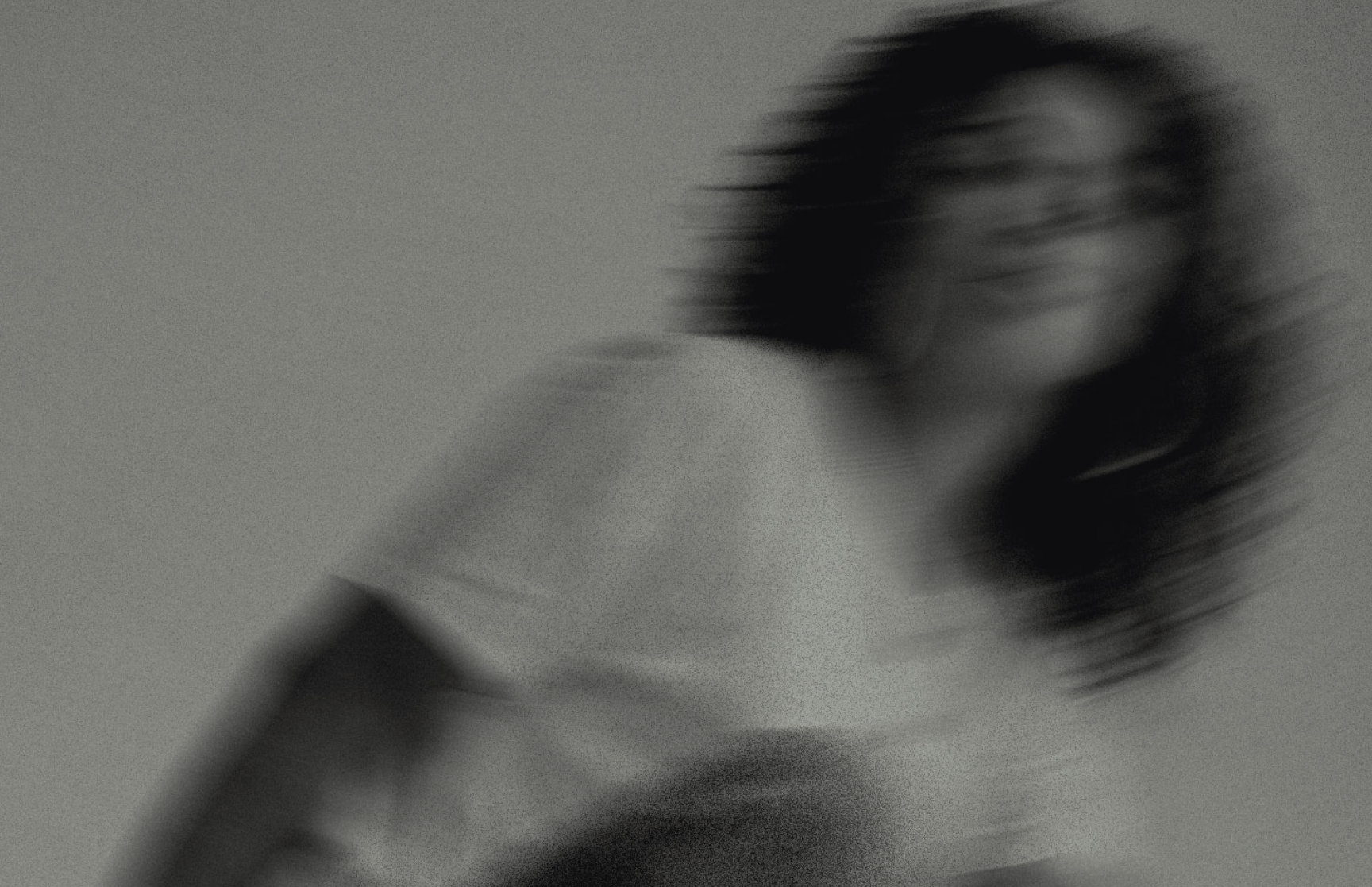 Blurry black and white photo of a person with shoulder-length hair wearing a light-colored shirt.