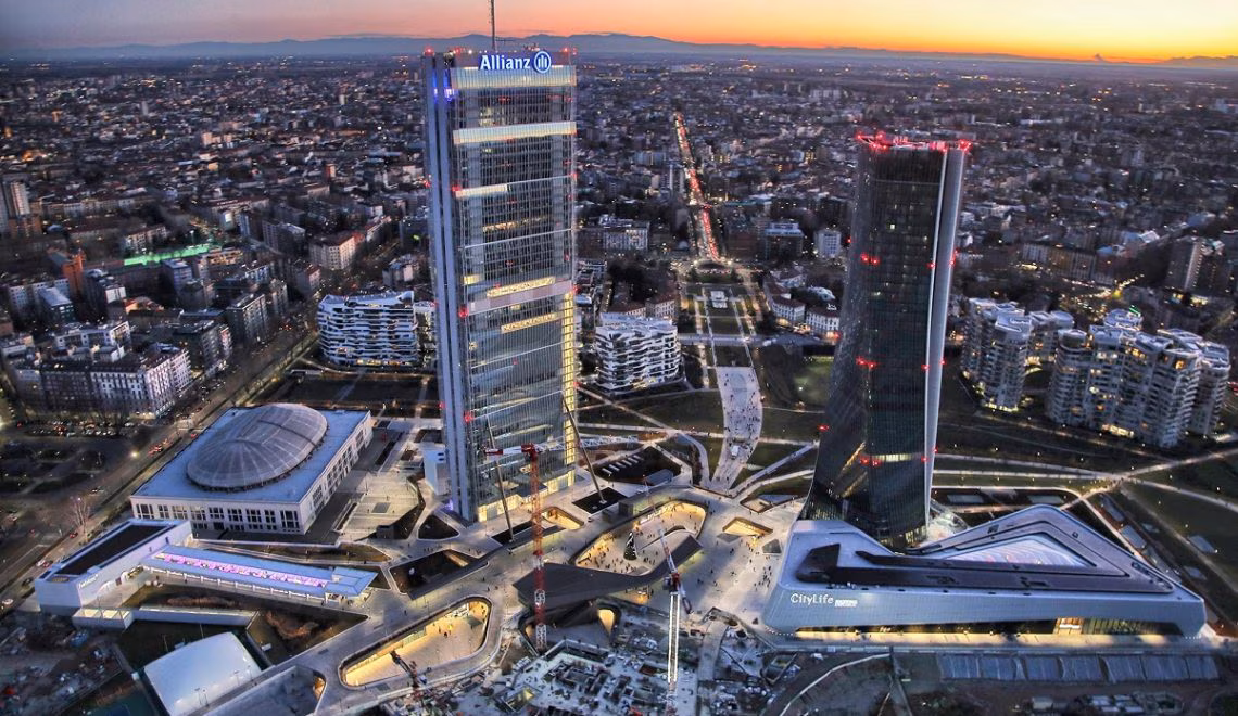 Aerial view of Milan skyline at dusk featuring tall buildings including the Allianz tower and the CityLife complex with city lights and streets.