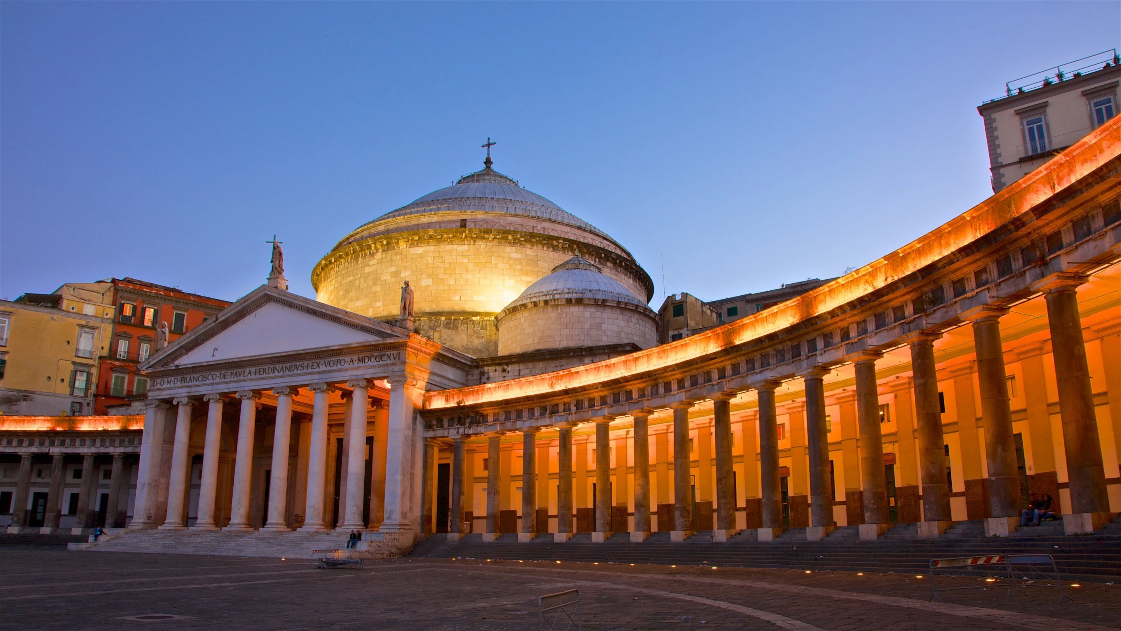 Evening view of Naples' Basilica of San Francesco di Paola with illuminated columns and a large dome against a clear sky.