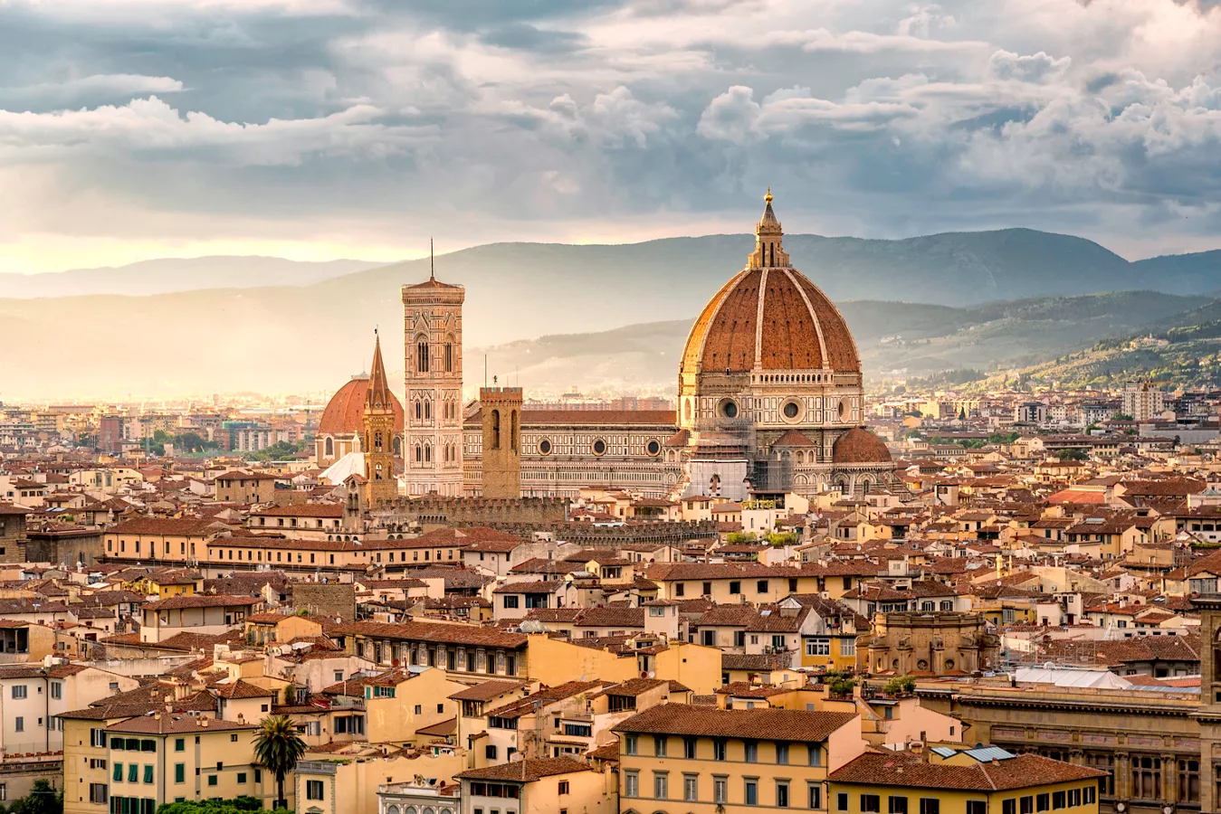 Panoramic view of Florence cityscape featuring the Florence Cathedral with its iconic dome and surrounding historic buildings under a cloudy sky.