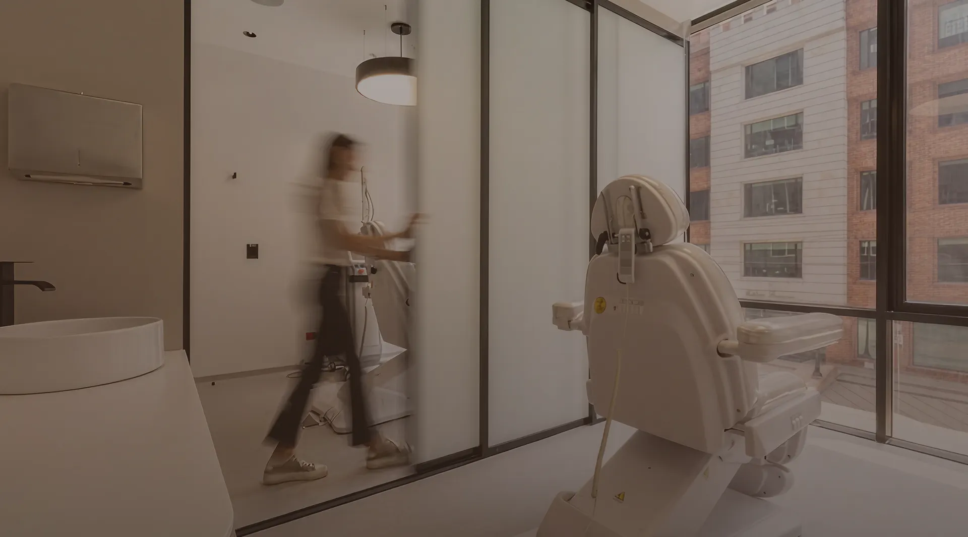 Modern medical or dental office with an adjustable chair and a person walking behind a frosted glass partition.