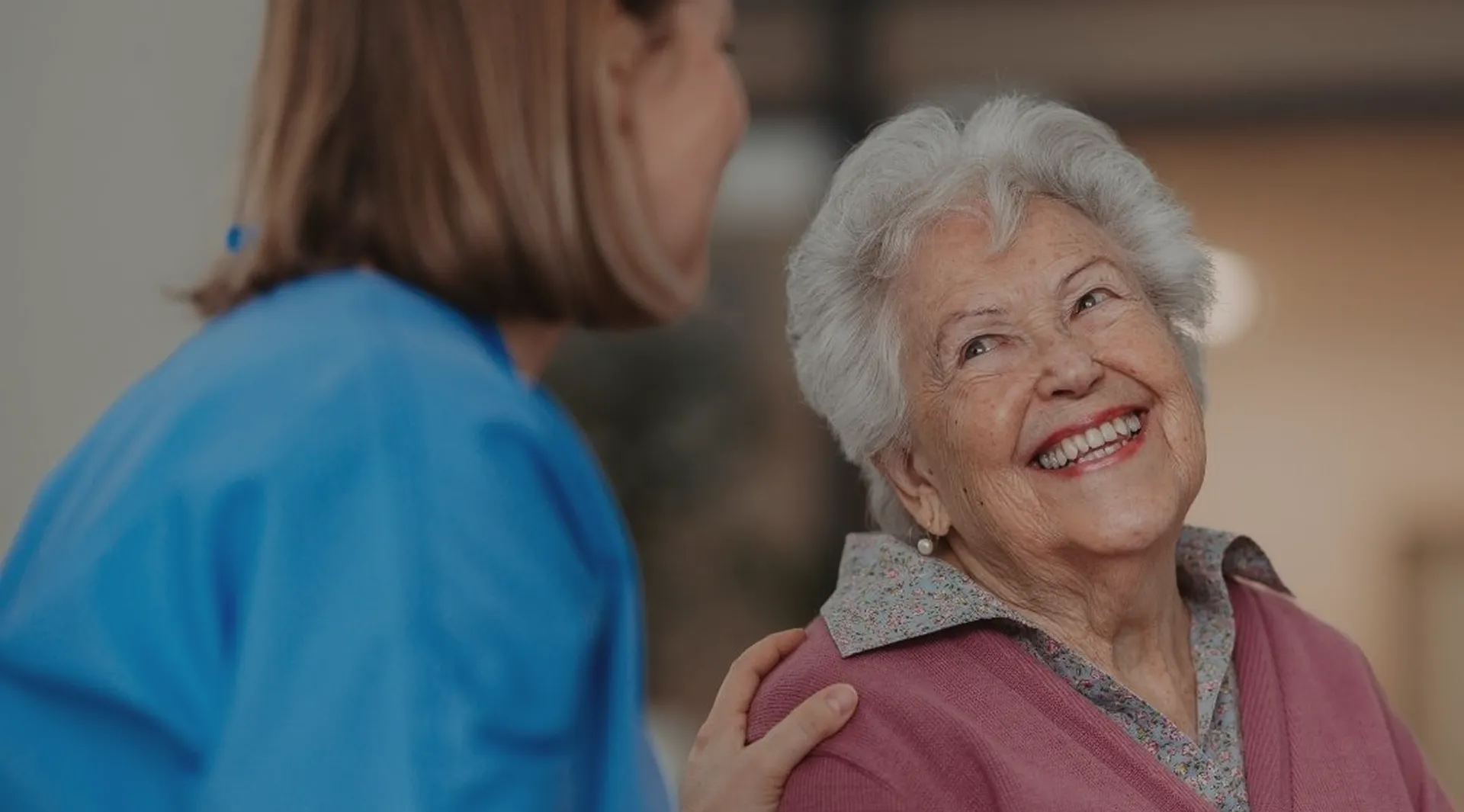Smiling elderly woman looking at a caregiver gently touching her shoulder.
