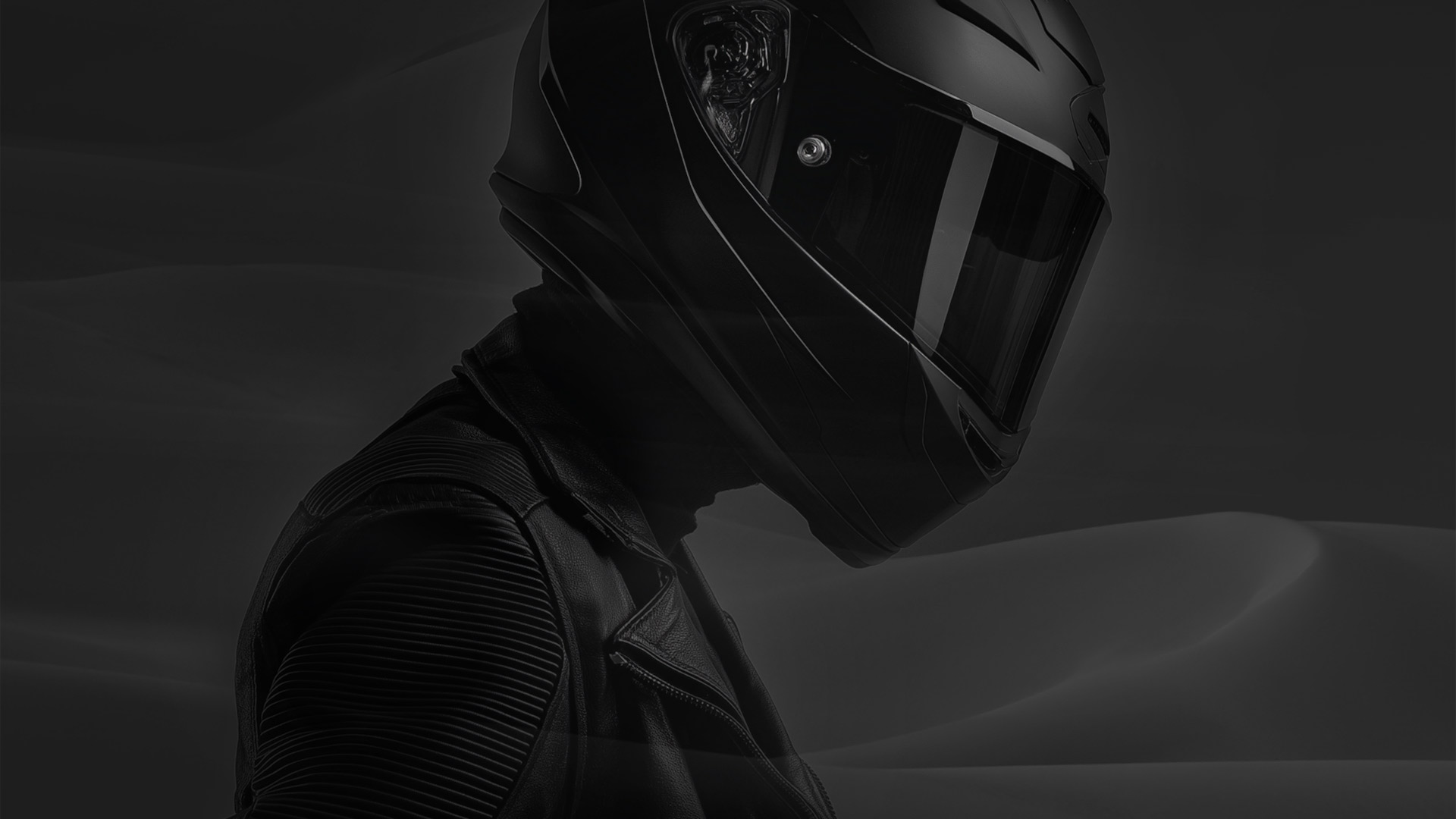 Profile of a person wearing a black motorcycle helmet and black leather jacket against a dark background.
