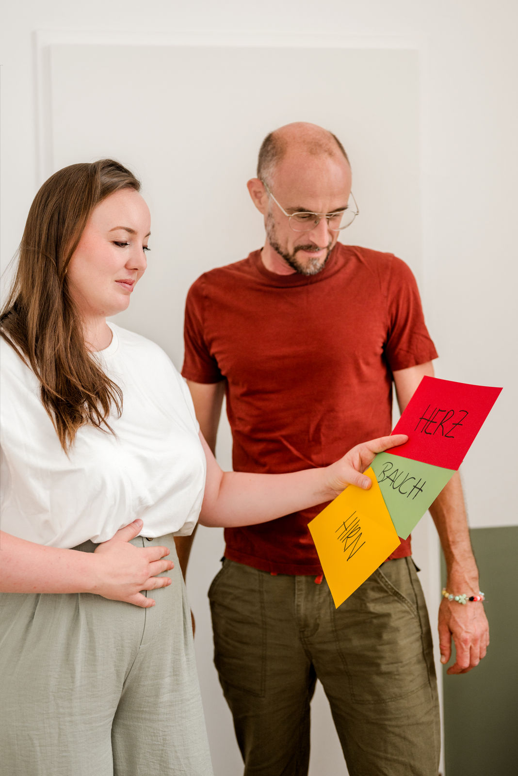 Sarah Lux und ein Kunde stehen im Praxisraum mit beschrifteten Kärtchen für "Bauch", "Herz" und "Hirn" für eine Einheit von Integrativer Körperarbeit in Bewegung.