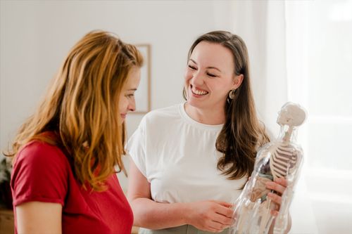 Sarah Lux und eine Kundin bei einer Einheit Somatic Education. Sie betrachten und zeigen auf ein Skelettmodell mit sichtbaren Organen.