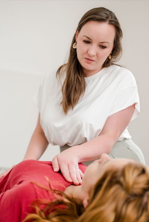 Sarah Lux legt die Hände auf eine liegende Kundin für eine integrative und achtsame Körperarbeit auf der Liege.
