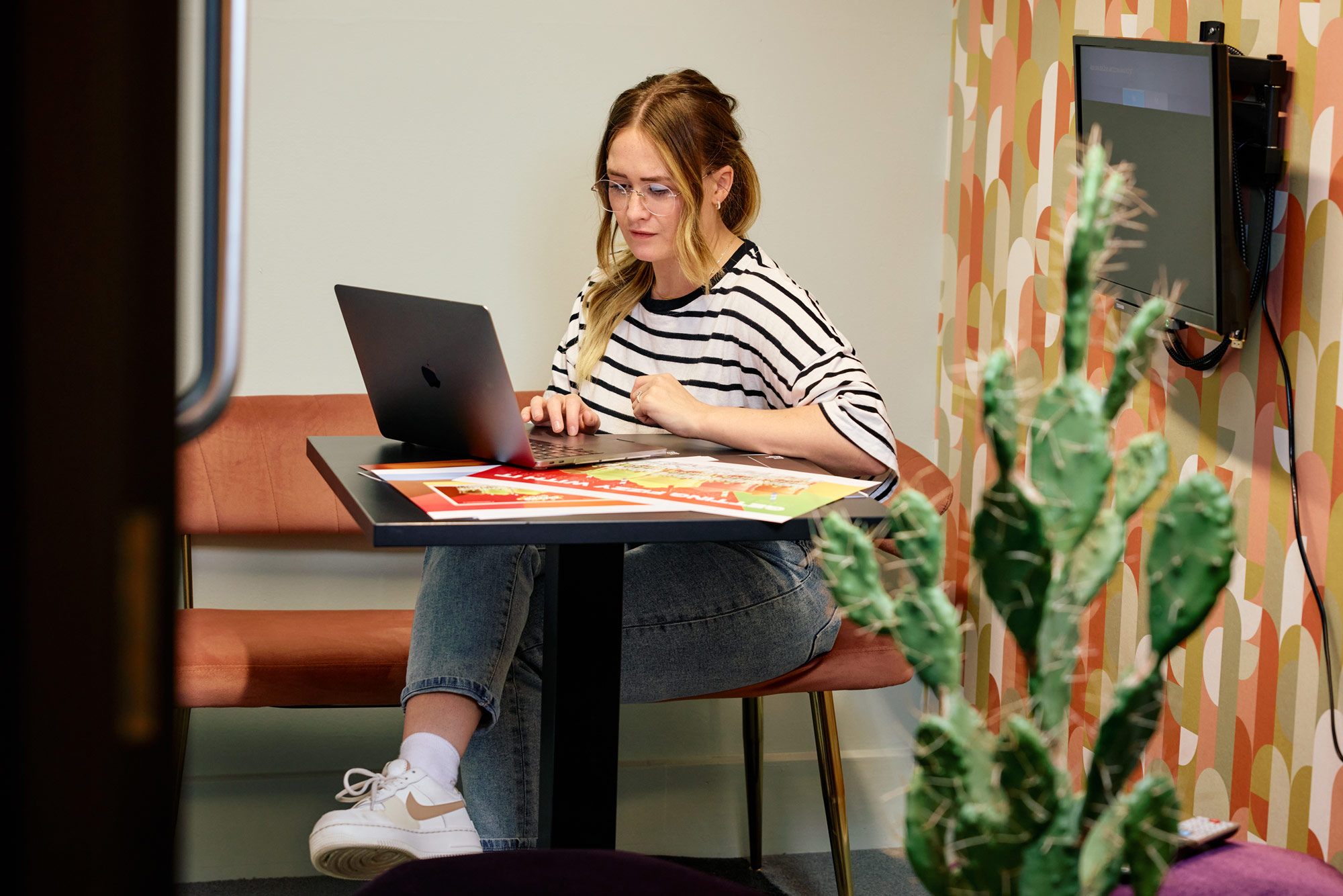 A designer working at a laptop with printed artwork in the studio booth