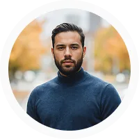 Portrait of a man with dark hair and beard wearing a navy blue turtleneck sweater against a blurred autumn background.