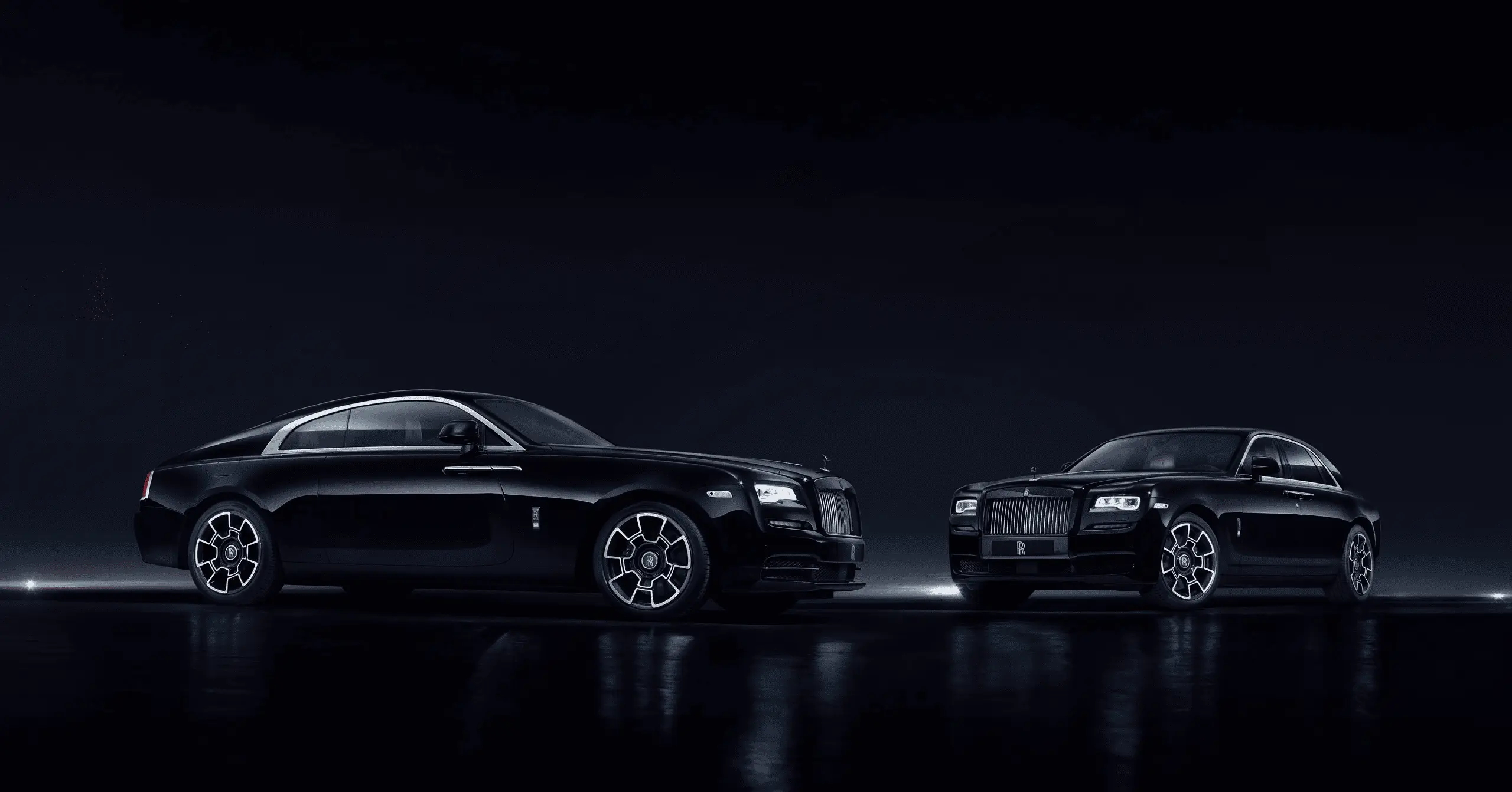 Deux voitures noires Rolls-Royce luxueuses garées sur une surface réfléchissante dans un environnement sombre.