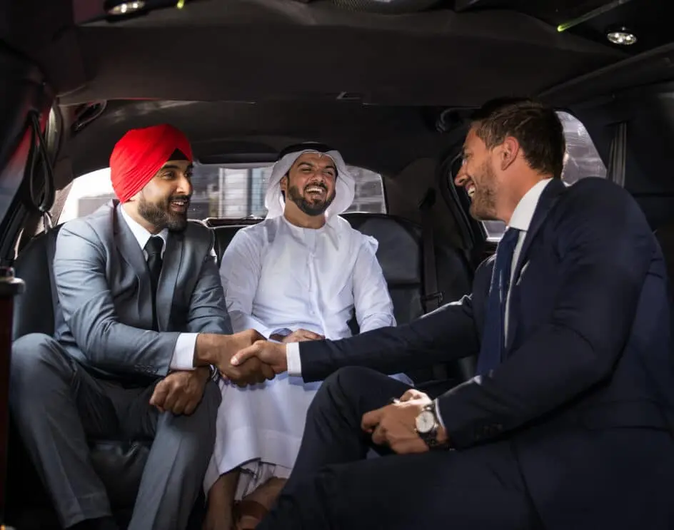 Trois hommes d'affaires diversifiés dans une voiture, deux se serrant la main et souriant.